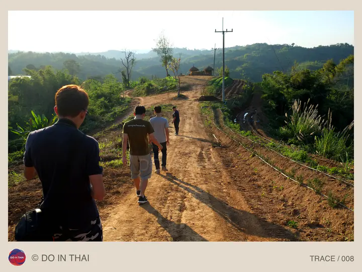 A group walks along a sunlit dirt road through the hills.