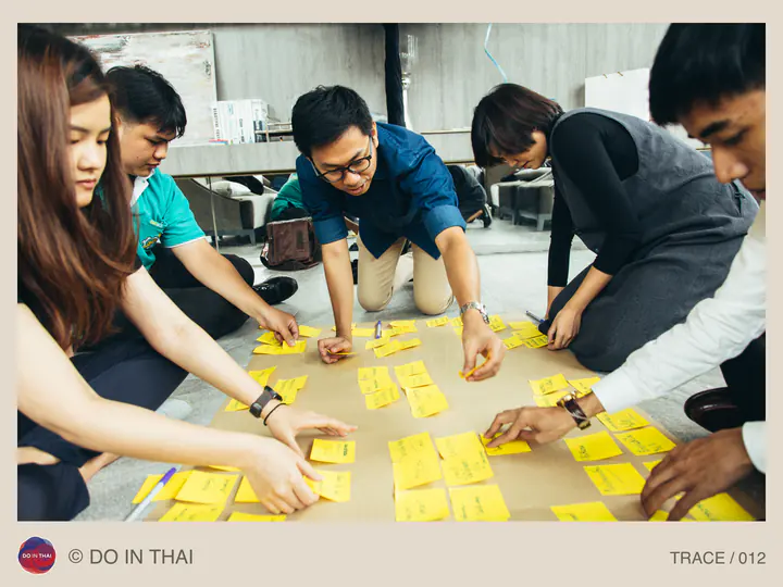 People lean over a table together, arranging yellow sticky notes.