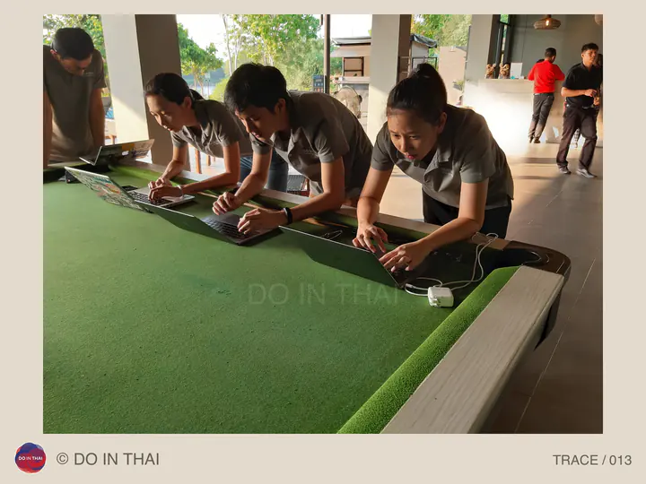 Team members work on laptops lined up along a long green table.