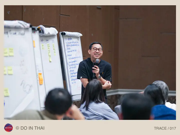 A speaker with a microphone sits beside flip charts covered in writing and notes.