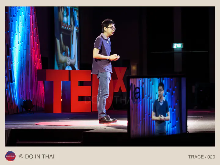 A speaker stands on a stage with TEDx letters and a foreground screen showing the talk.