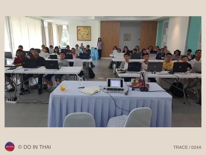 Participants face the camera from rows of tables with open laptops in a bright training room.