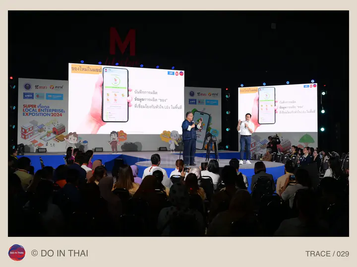 A presenter speaks on stage in front of large phone-app slides and a seated audience.