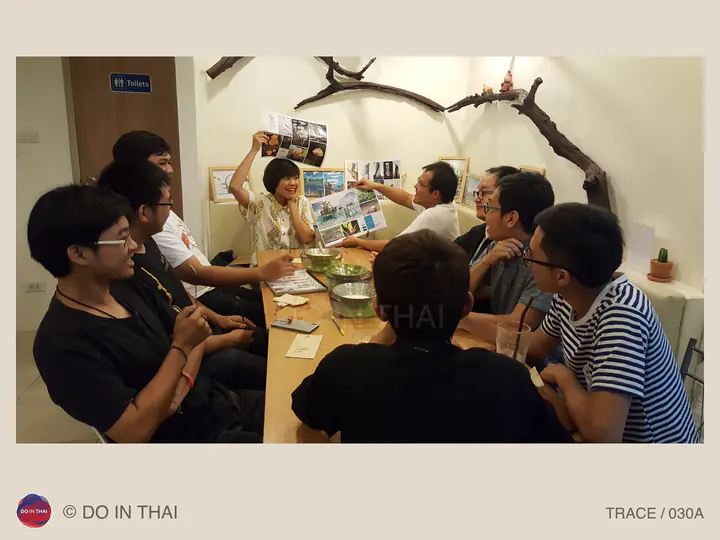 People gather around a wooden table as one person holds up printed photographs and another points to them.
