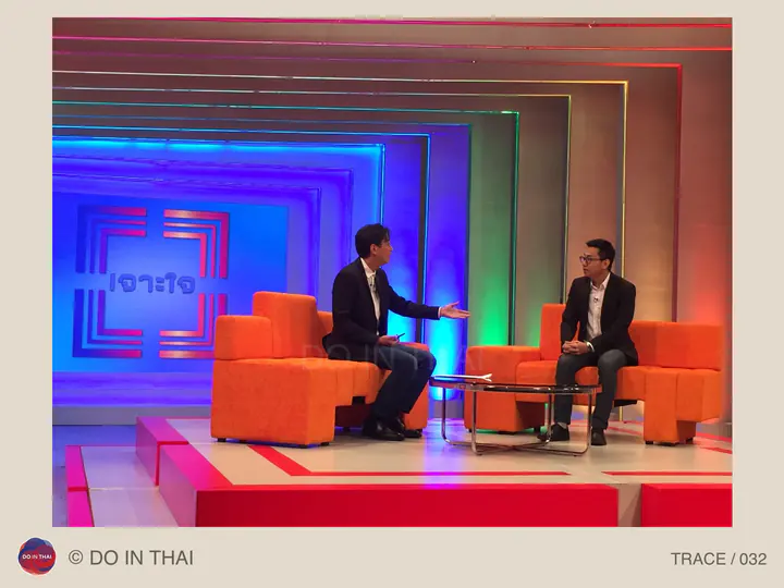 Two people talk in orange armchairs in a brightly coloured television studio.