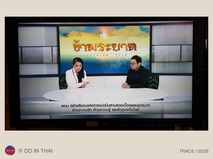 A photograph of a television screen showing two people in conversation on Lightning Talk, with Thai captions below.