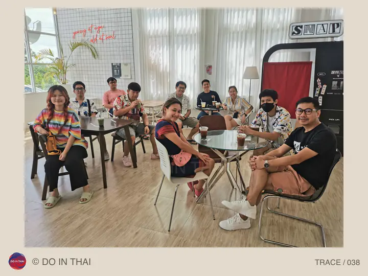 A group sits around tables in a bright café with windows and plants.