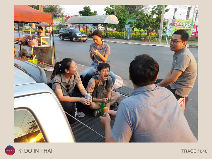 A team chats and shares snacks around a pickup truck’s tailgate beside a road.