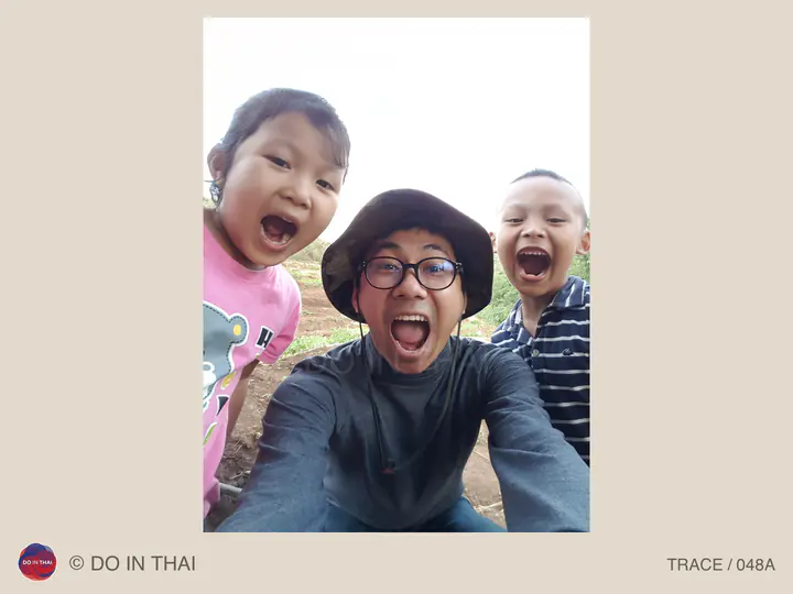 A person wearing glasses and a sun hat takes an outdoor selfie with two children, all making playful open-mouthed expressions.